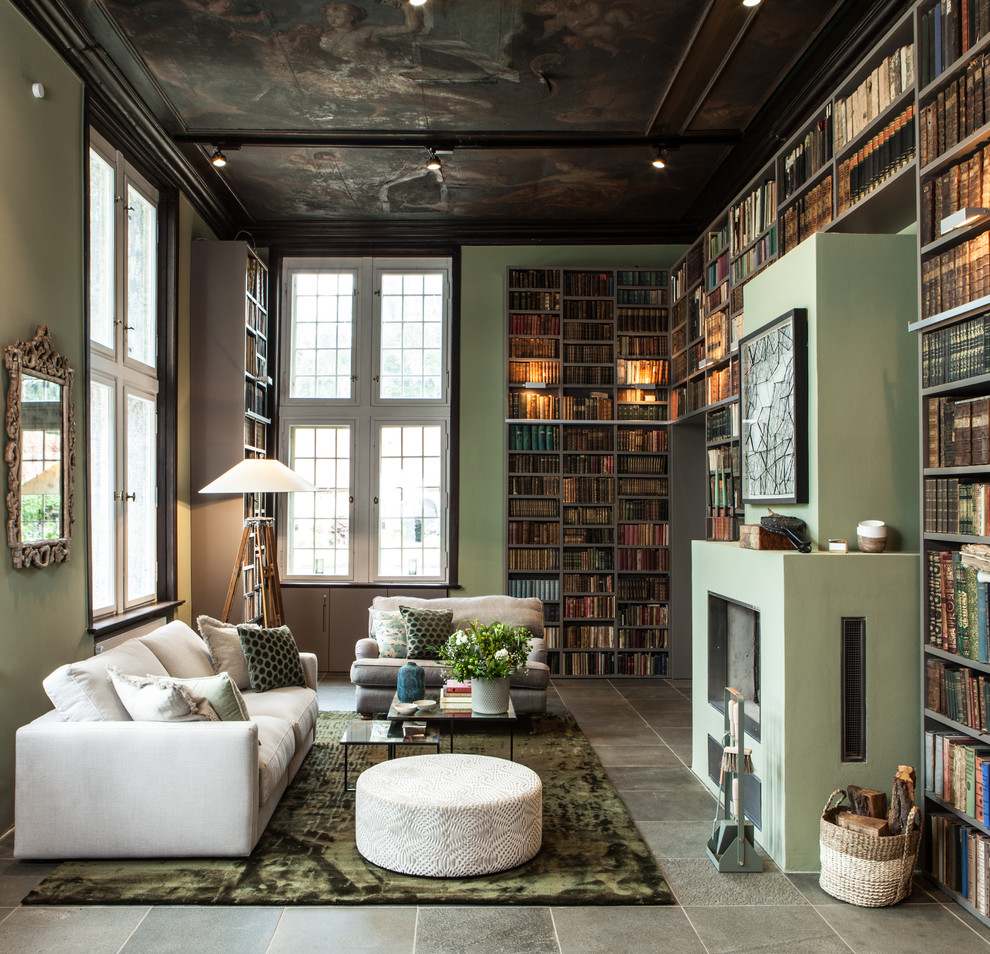 На фото: большая двухуровневая гостиная комната в современном стиле с с книжными шкафами и полками, зелеными стенами, фасадом камина из штукатурки, горизонтальным камином и серым полом без телевизора