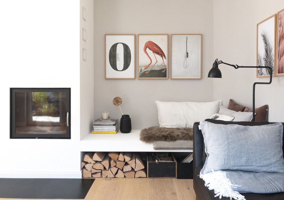 Diseño de sala de estar abierta escandinava de tamaño medio sin televisor con paredes grises, suelo de madera clara, estufa de leña y marco de chimenea de yeso