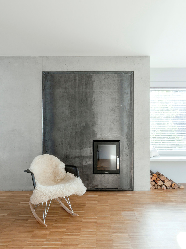 Inspiration pour un salon nordique avec un mur gris, un sol en bois brun, une cheminée standard, un manteau de cheminée en métal et un sol marron.