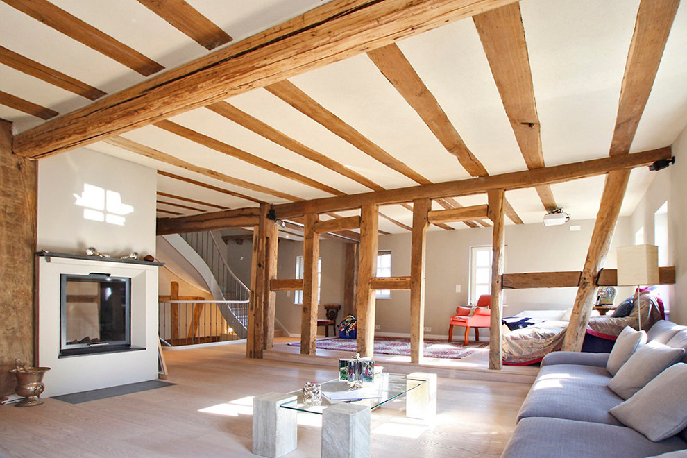 Modelo de salón abierto actual grande sin televisor con paredes grises, suelo de madera clara y chimenea de doble cara