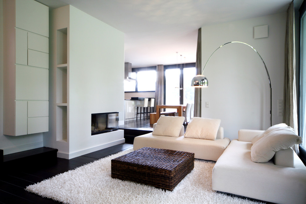 Cette photo montre une salle de séjour tendance de taille moyenne et ouverte avec une cheminée d'angle, un mur blanc, parquet foncé et un manteau de cheminée en plâtre.