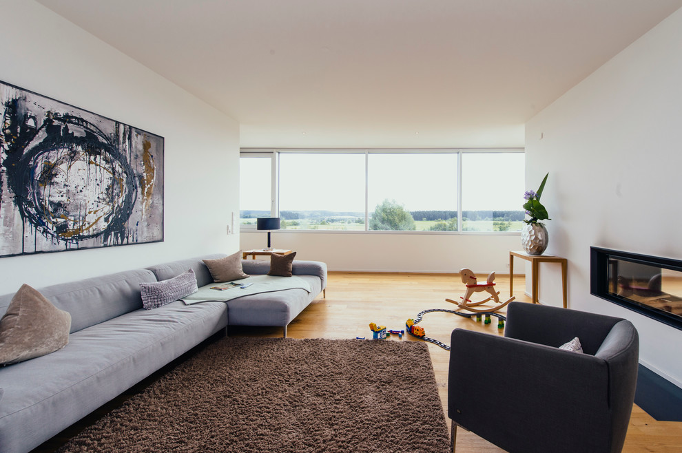 Ejemplo de sala de estar abierta actual de tamaño medio sin televisor con paredes blancas, suelo de madera en tonos medios, chimenea de doble cara y marco de chimenea de yeso