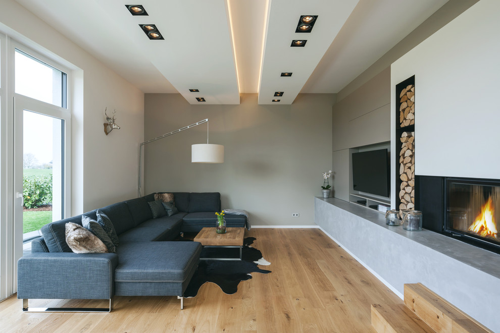 Idées déco pour un salon contemporain fermé et de taille moyenne avec un mur beige, parquet clair, une cheminée standard, un manteau de cheminée en plâtre, un téléviseur encastré et un sol beige.