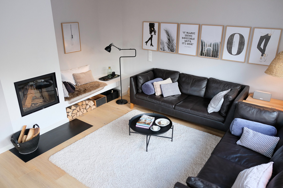 Modelo de sala de estar abierta nórdica de tamaño medio sin televisor con paredes grises, suelo de madera clara, estufa de leña y marco de chimenea de yeso