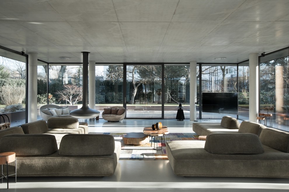 Ispirazione per un ampio soggiorno industriale stile loft con pavimento in cemento, camino sospeso, TV a parete e pavimento grigio