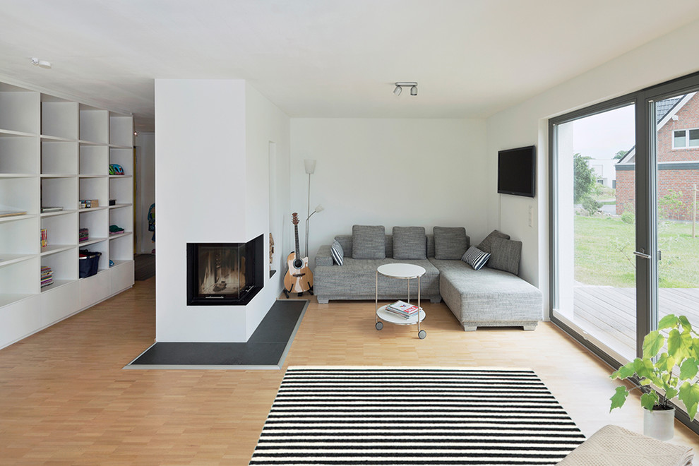 Bild på ett nordiskt vardagsrum, med vita väggar, ljust trägolv, en spiselkrans i metall och en väggmonterad TV