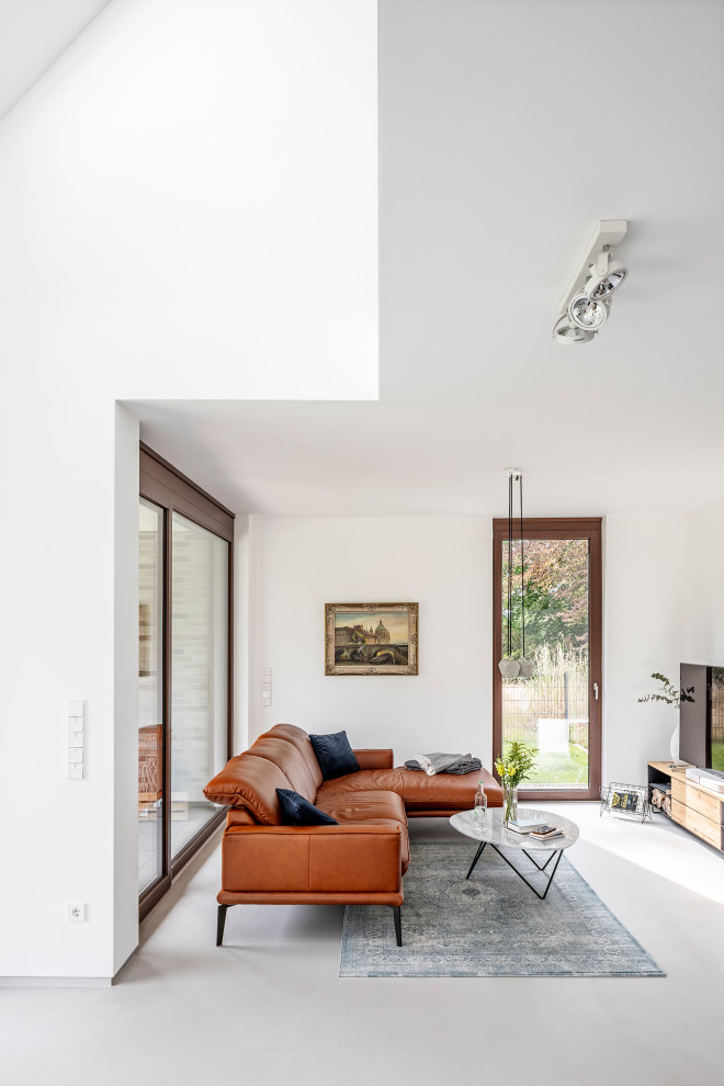 Offenes Modernes Wohnzimmer mit weißer Wandfarbe, Betonboden, freistehendem TV und grauem Boden in Sonstige