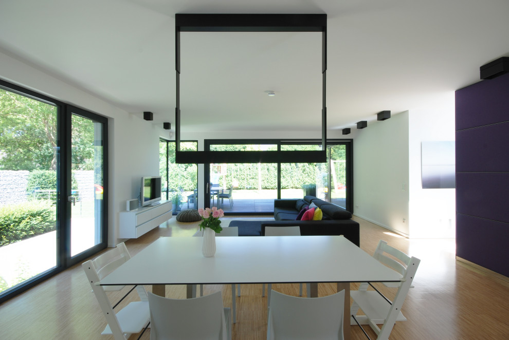 Imagen de salón abierto minimalista grande sin chimenea con paredes blancas, suelo de bambú, televisor colgado en la pared y suelo beige