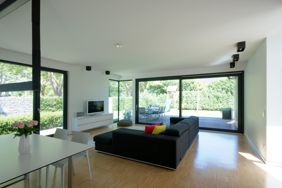Immagine di un grande soggiorno minimalista aperto con pareti bianche, pavimento in bambù, nessun camino, TV a parete e pavimento beige