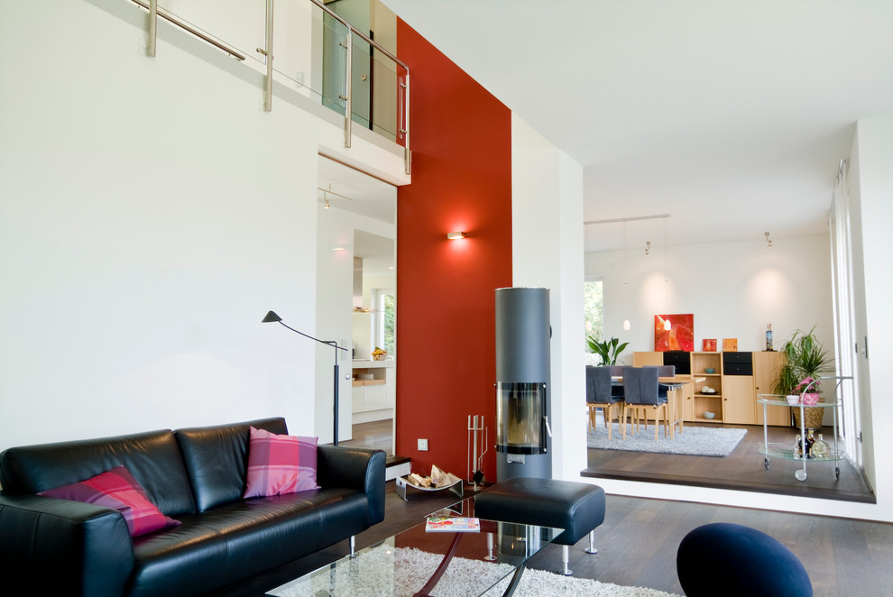 This is an example of a large contemporary formal open plan living room feature wall in Essen with dark hardwood flooring, a wood burning stove and red walls.