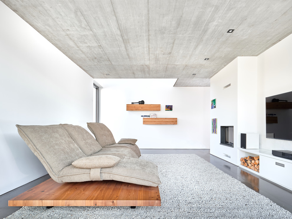На фото: изолированная гостиная комната в современном стиле с стандартным камином, фасадом камина из штукатурки, белыми стенами, телевизором на стене и серым полом с