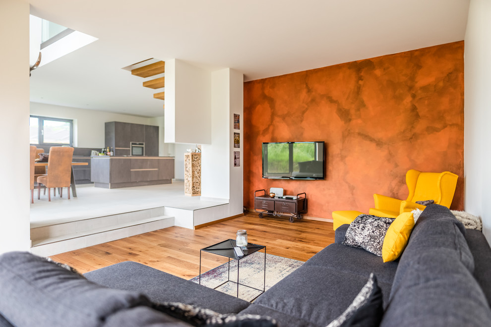 Mittelgroßes, Offenes Modernes Wohnzimmer mit weißer Wandfarbe, braunem Holzboden, TV-Wand und braunem Boden in Sonstige