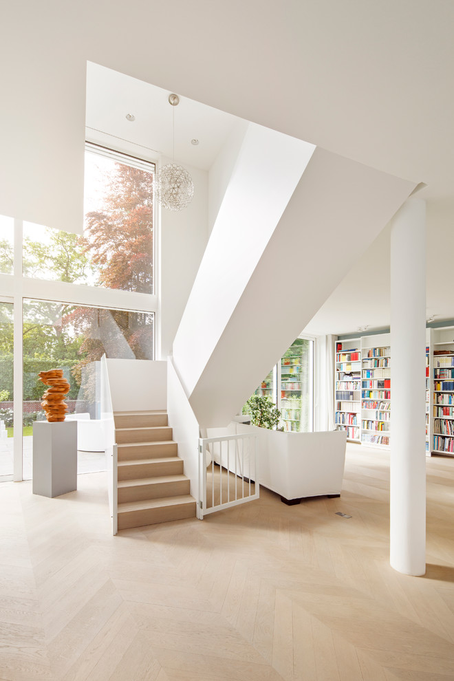 Réalisation d'un grand salon design ouvert avec une bibliothèque ou un coin lecture, un mur blanc et parquet clair.