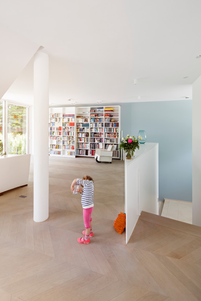 Imagen de biblioteca en casa abierta actual grande con paredes azules y suelo de madera clara