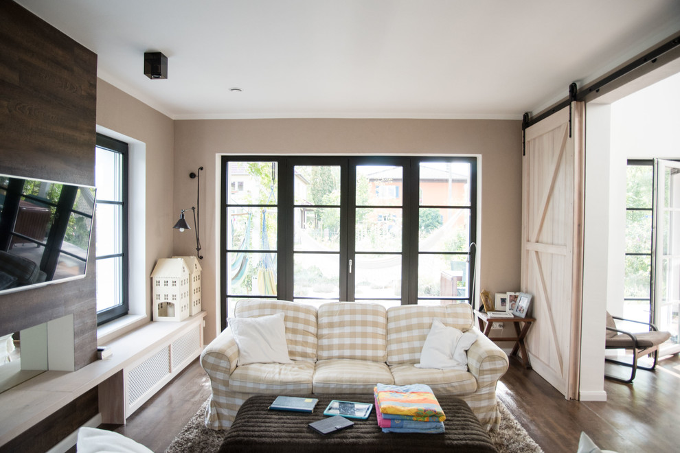 Diseño de sala de estar cerrada campestre de tamaño medio sin chimenea con paredes beige, suelo de madera oscura y televisor colgado en la pared