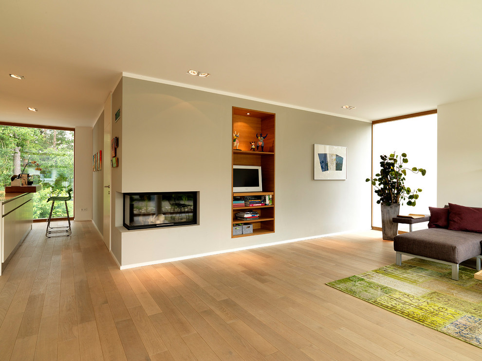 Großes, Offenes Modernes Wohnzimmer mit grauer Wandfarbe, braunem Holzboden, Eckkamin, verputzter Kaminumrandung und freistehendem TV in Nürnberg