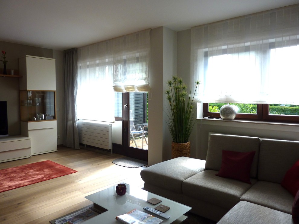 Cette photo montre une salle de séjour tendance de taille moyenne et ouverte avec un mur beige, parquet clair, une cheminée d'angle, un manteau de cheminée en plâtre et un téléviseur indépendant.