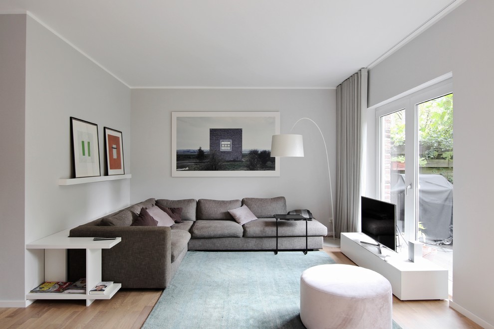 Kleines, Abgetrenntes Modernes Wohnzimmer ohne Kamin mit grauer Wandfarbe, braunem Holzboden, freistehendem TV und braunem Boden in Düsseldorf