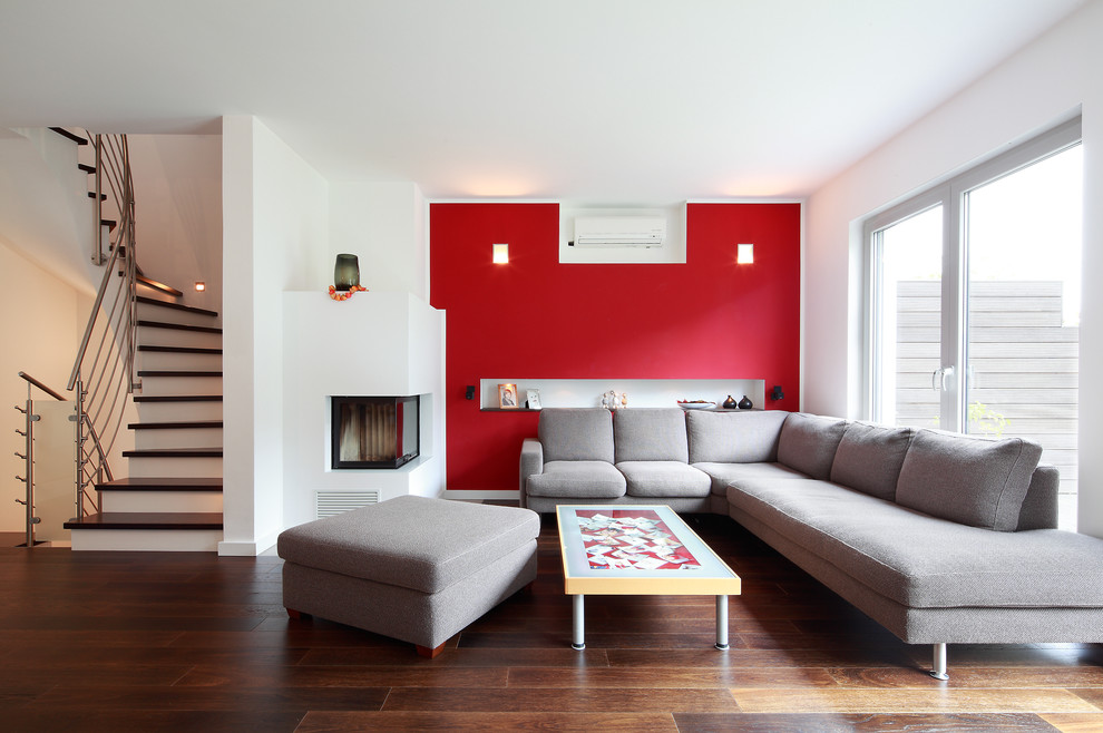 На фото: парадная, открытая гостиная комната среднего размера в современном стиле с красными стенами, темным паркетным полом и фасадом камина из штукатурки без телевизора