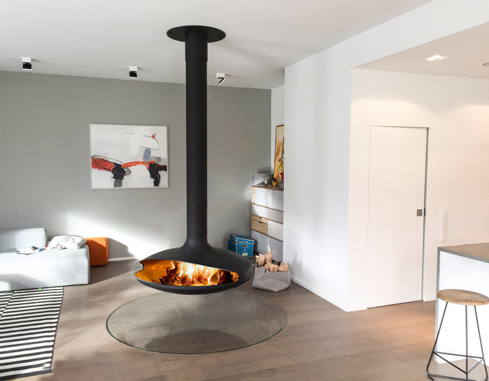 Diseño de salón nórdico de tamaño medio con paredes grises, suelo de madera en tonos medios y chimeneas suspendidas