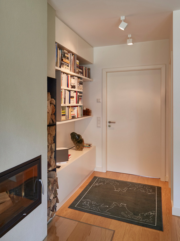 Пример оригинального дизайна: открытая гостиная комната в современном стиле с белыми стенами, светлым паркетным полом, коричневым полом, с книжными шкафами и полками, угловым камином и фасадом камина из штукатурки