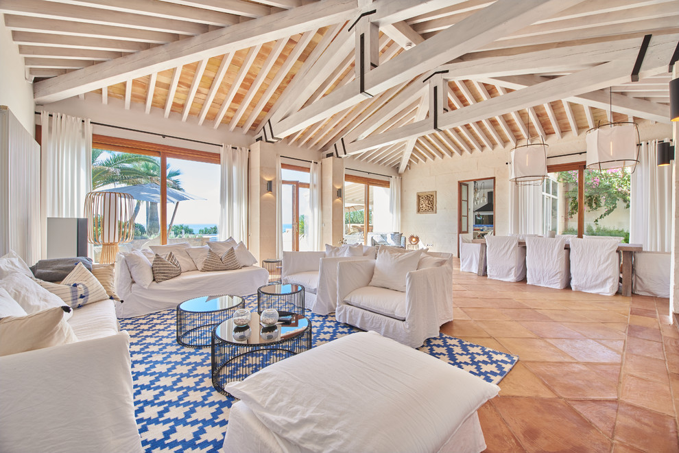 Inspiration for a beach style open plan living room in Palma de Mallorca with terracotta flooring, white walls, a corner fireplace, a metal fireplace surround and brown floors.