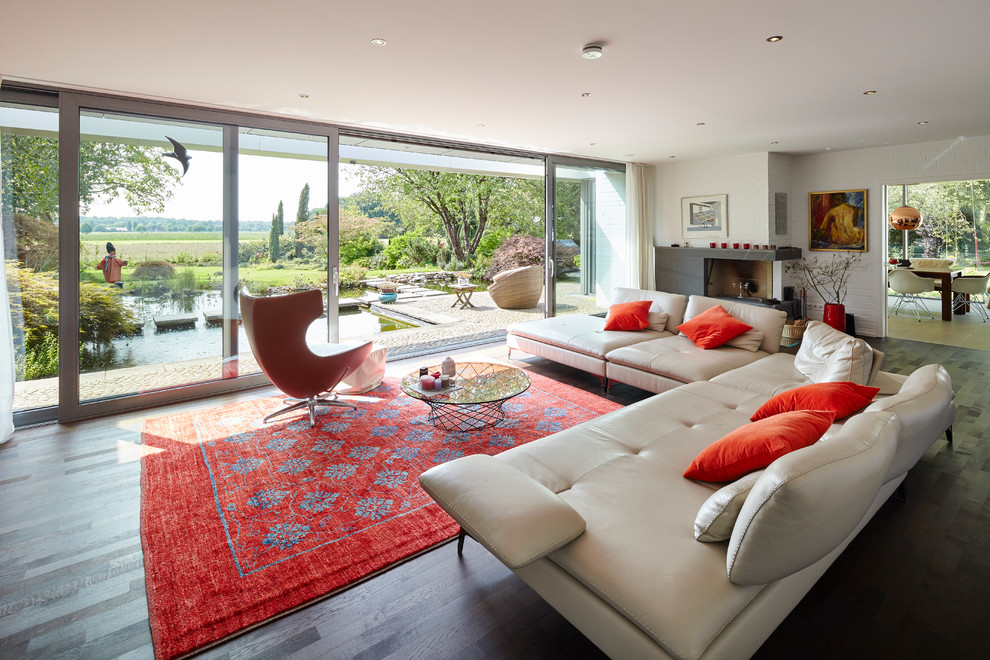 Immagine di un grande soggiorno minimal aperto con sala formale, pareti bianche, pavimento in legno verniciato, camino ad angolo e pavimento marrone