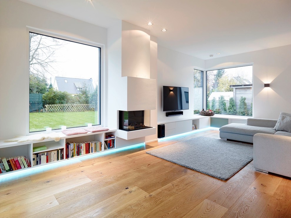 Idee per un grande soggiorno moderno chiuso con pareti bianche, pavimento in legno massello medio, cornice del camino in intonaco e TV a parete
