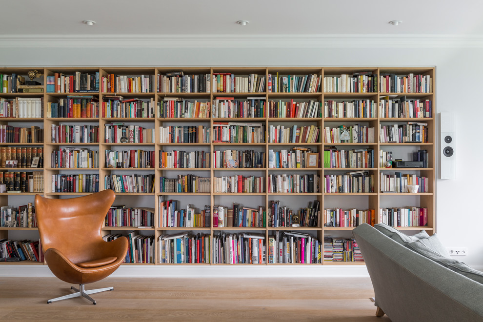 Imagen de sala de estar con biblioteca abierta actual de tamaño medio sin chimenea y televisor con paredes blancas, suelo de madera clara y suelo marrón