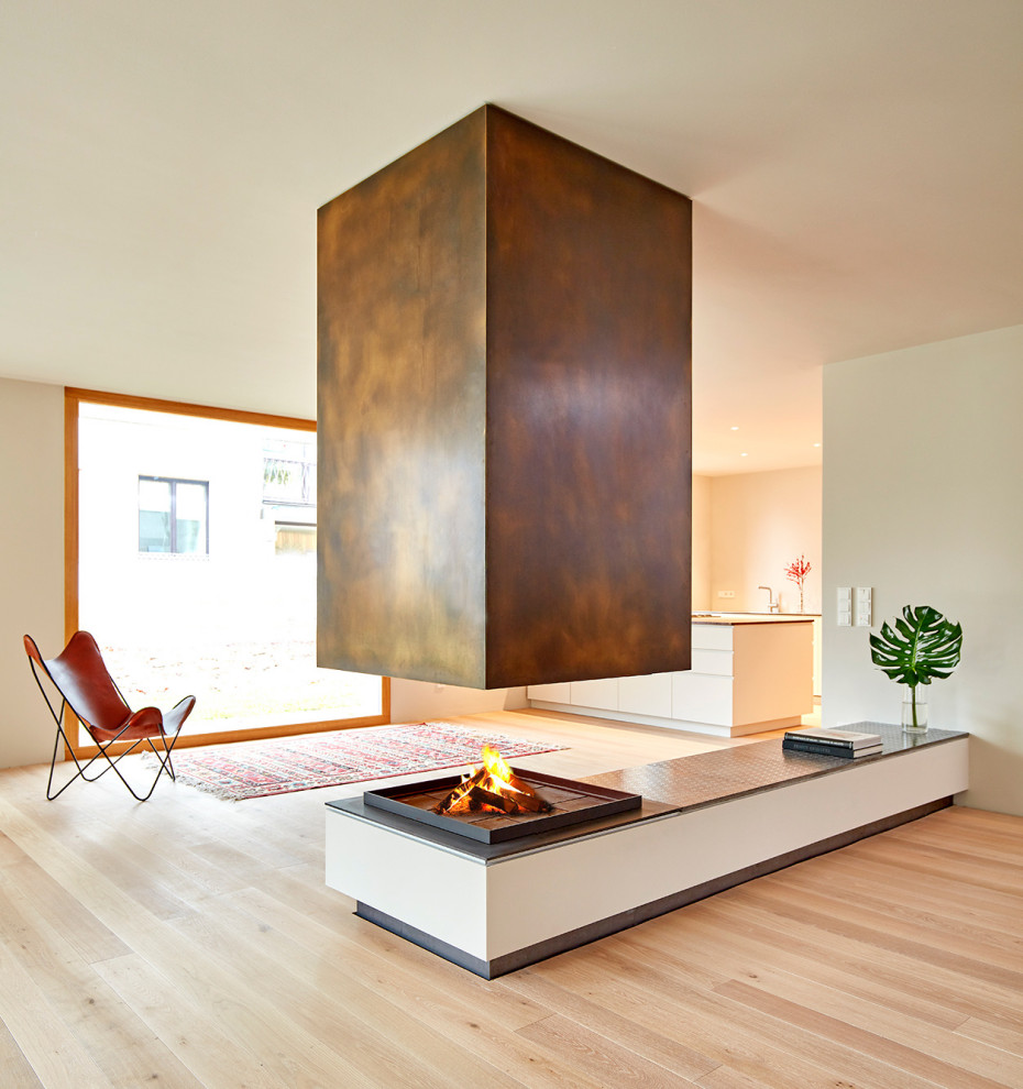 Diseño de sala de estar abierta actual grande con suelo de madera clara, chimenea de doble cara, marco de chimenea de metal y suelo beige