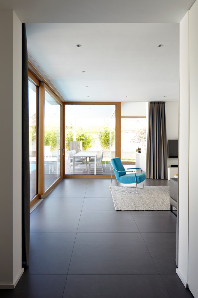 Offenes Modernes Wohnzimmer ohne Kamin mit weißer Wandfarbe, TV-Wand und schwarzem Boden in Köln