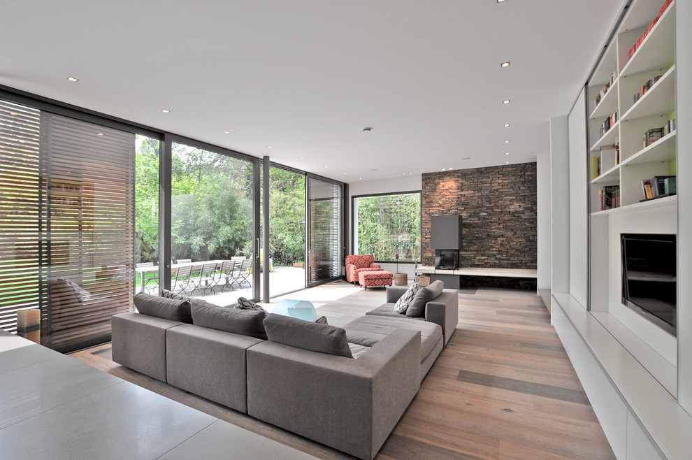 Идея дизайна: большая открытая гостиная комната в современном стиле с деревянным полом и телевизором на стене