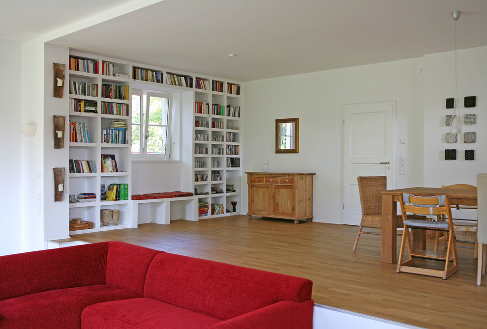 Bild på ett mellanstort minimalistiskt allrum med öppen planlösning, med ett bibliotek, vita väggar, mellanmörkt trägolv, en öppen vedspis, en spiselkrans i metall, en dold TV och brunt golv