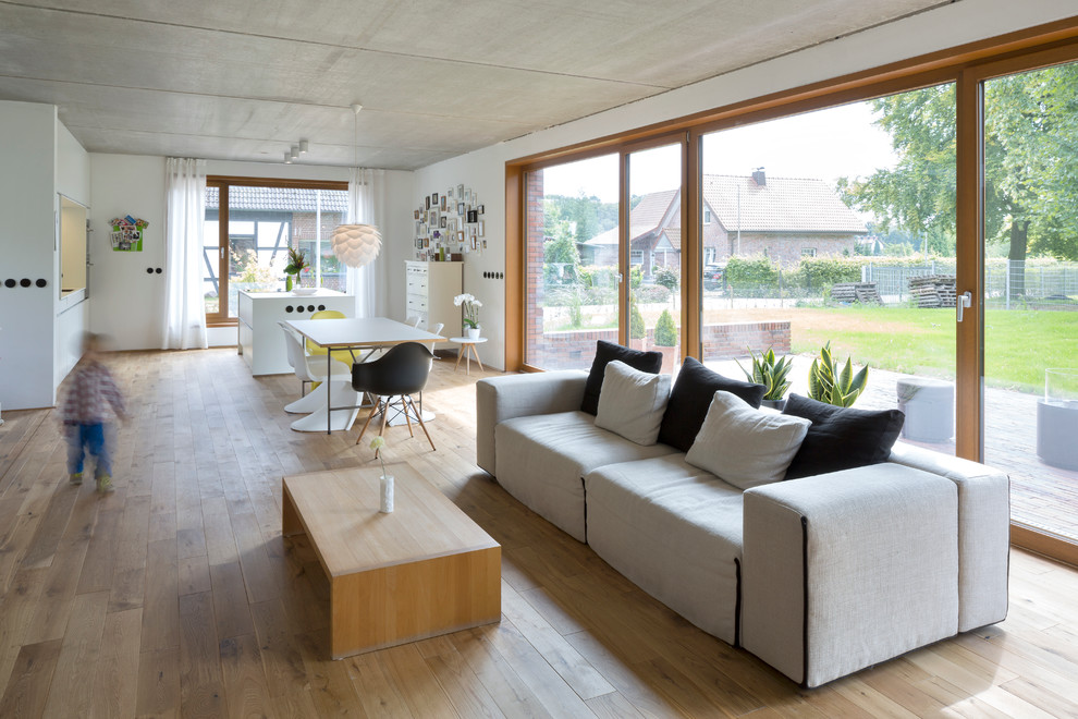 Mittelgroßes, Offenes Modernes Wohnzimmer ohne Kamin mit weißer Wandfarbe und braunem Holzboden in Dortmund