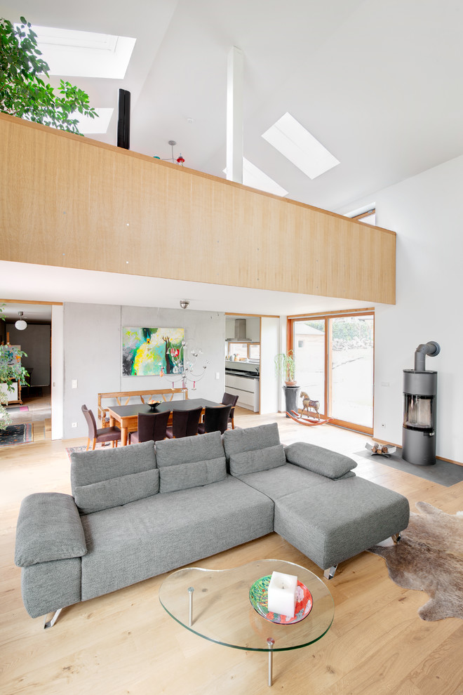 Bild på ett stort minimalistiskt vardagsrum, med vita väggar, ljust trägolv och en öppen vedspis