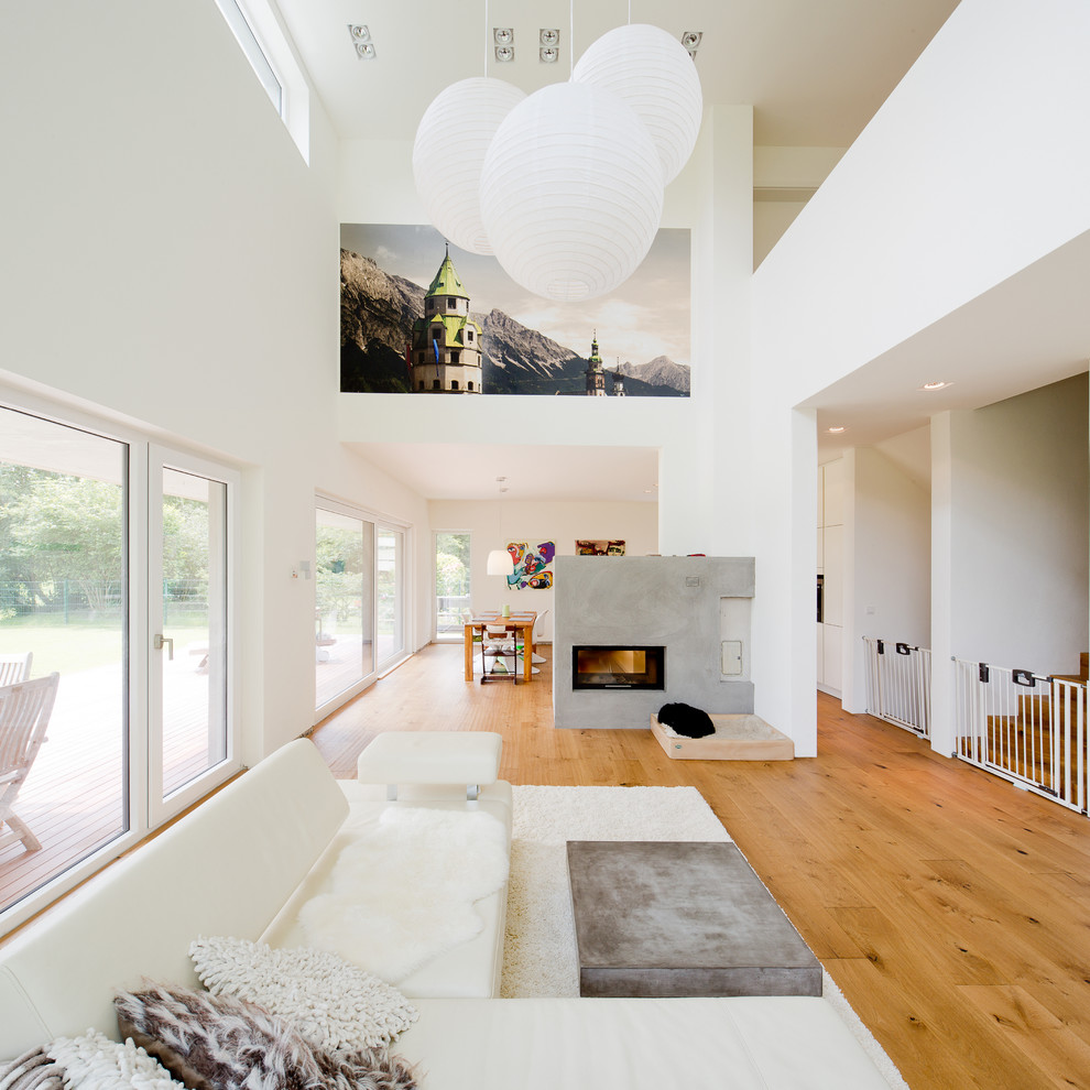 Ejemplo de sala de estar abierta moderna grande con paredes blancas, suelo de madera en tonos medios, chimenea lineal y marco de chimenea de hormigón