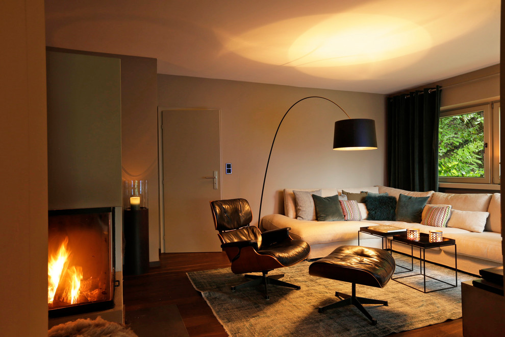 Imagen de sala de estar abierta actual pequeña con paredes beige, suelo de madera oscura, chimenea de esquina, marco de chimenea de yeso y suelo marrón