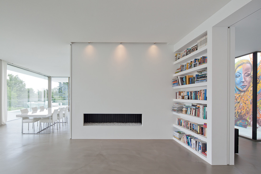 Foto de sala de estar con biblioteca abierta contemporánea con paredes blancas, suelo de cemento, chimenea lineal y marco de chimenea de yeso
