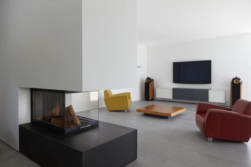 他の地域にある広いコンテンポラリースタイルのおしゃれな独立型リビング (両方向型暖炉、白い壁、スレートの床、石材の暖炉まわり、壁掛け型テレビ) の写真