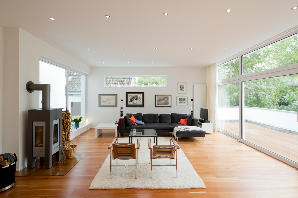 Bild på ett stort minimalistiskt allrum med öppen planlösning, med ett finrum, vita väggar, ljust trägolv, en öppen vedspis och en fristående TV