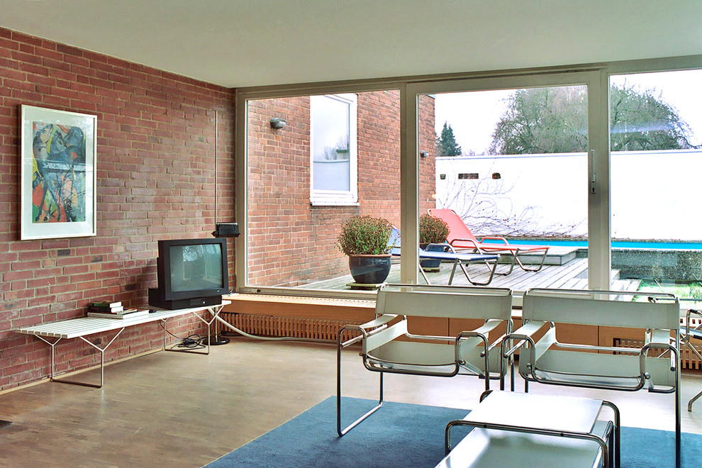 Стильный дизайн: изолированная гостиная комната среднего размера в современном стиле с отдельно стоящим телевизором, красными стенами и паркетным полом среднего тона без камина - последний тренд
