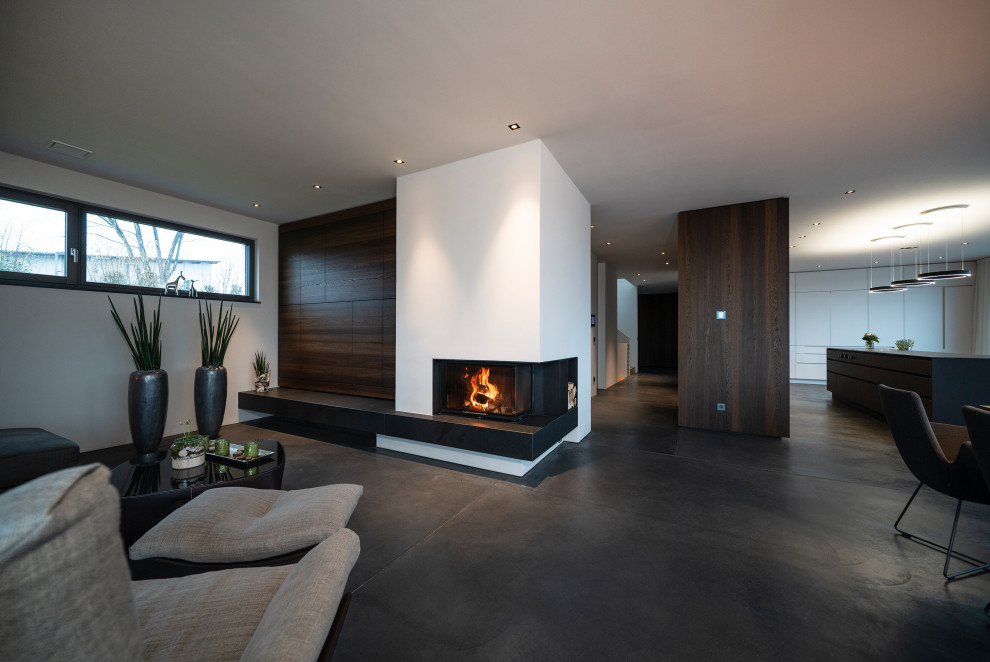 シュトゥットガルトにある高級な広いコンテンポラリースタイルのおしゃれなLDK (白い壁、コンクリートの床、コーナー設置型暖炉、漆喰の暖炉まわり、内蔵型テレビ、グレーの床) の写真