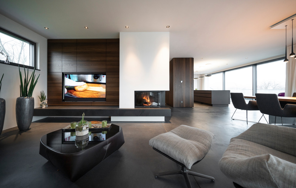 Идея дизайна: большая открытая гостиная комната в современном стиле с белыми стенами, бетонным полом, угловым камином, фасадом камина из штукатурки, скрытым телевизором и серым полом