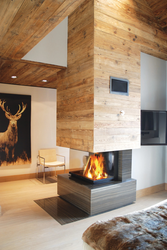 Immagine di un soggiorno design con pareti bianche, camino bifacciale, cornice del camino in legno e TV a parete