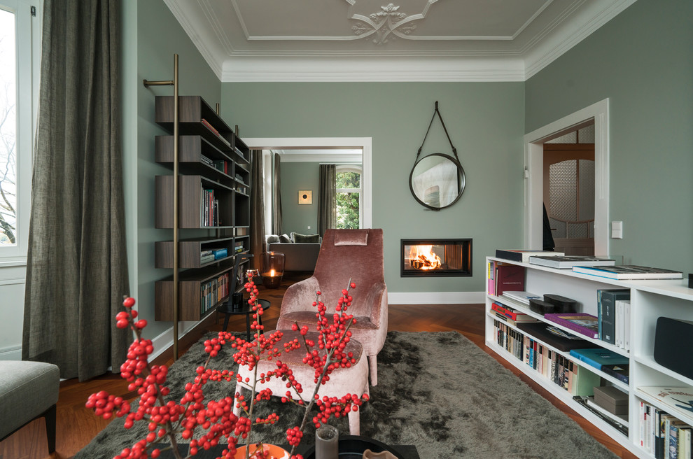 Cette image montre un grand salon traditionnel ouvert avec une cheminée double-face, un manteau de cheminée en plâtre, une salle de réception, un mur vert, un sol en bois brun, un sol marron et aucun téléviseur.