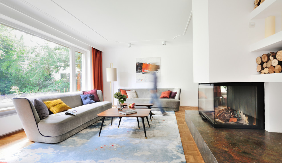 Cette image montre une grande salle de séjour vintage ouverte avec un mur blanc, un sol en bois brun, un manteau de cheminée en plâtre, aucun téléviseur, un sol marron et une cheminée double-face.
