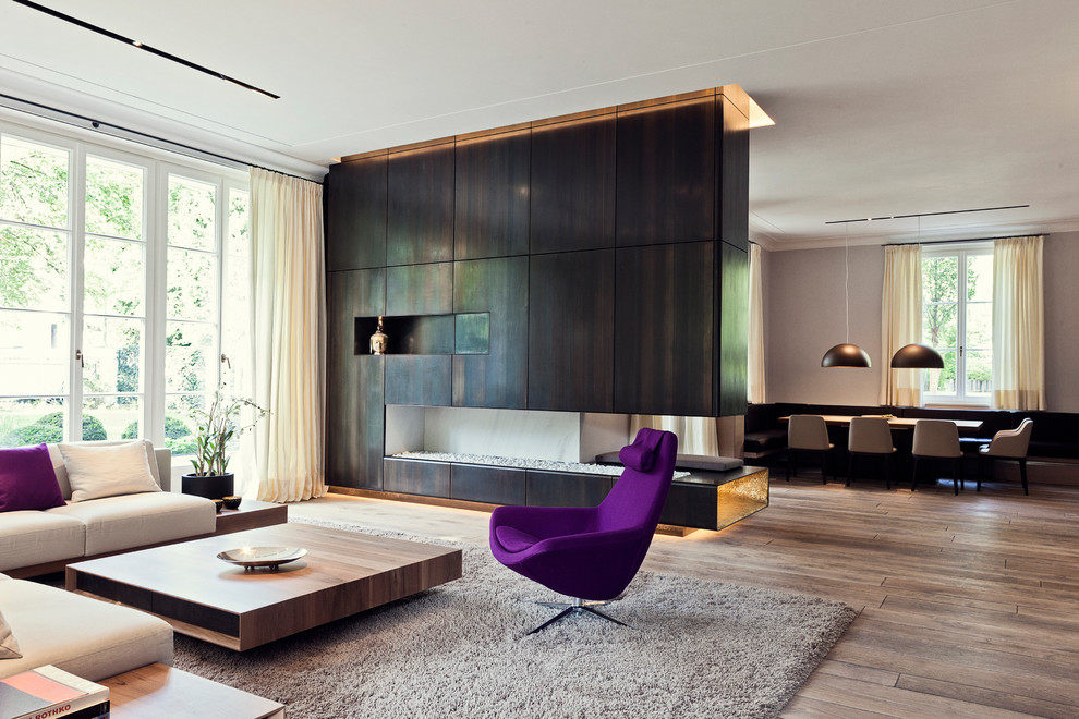 Idée de décoration pour un grand salon design ouvert avec un sol en bois brun, cheminée suspendue, un manteau de cheminée en métal, un téléviseur dissimulé et un mur beige.
