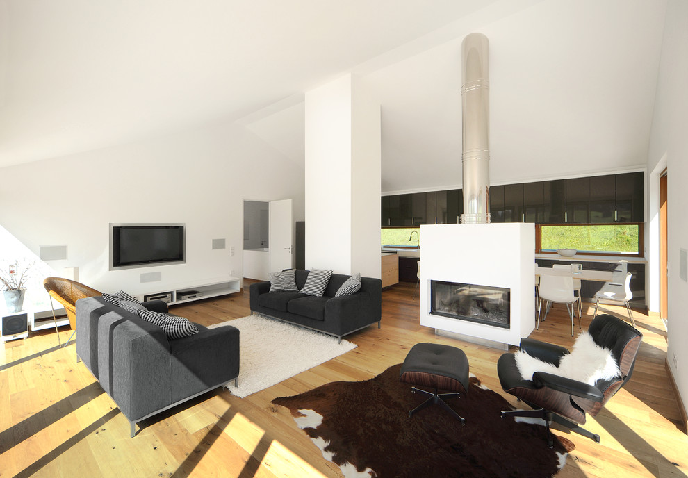 Diseño de sala de estar abierta contemporánea extra grande con paredes blancas, suelo de madera en tonos medios, chimenea de doble cara, televisor colgado en la pared y marco de chimenea de yeso