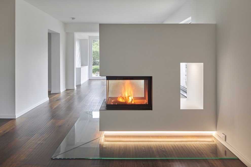 Modelo de salón abierto minimalista extra grande con paredes blancas, suelo de madera oscura, chimenea de doble cara y marco de chimenea de yeso