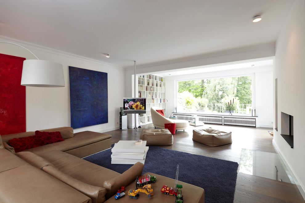 This is an example of a large contemporary open plan games room in Essen with white walls, dark hardwood flooring, a plastered fireplace surround, a freestanding tv and a standard fireplace.